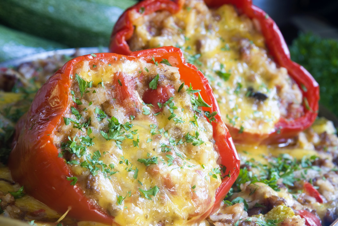 Red bell peppers stuffed with rice, tomatoes, and cheese; shot in natural light.