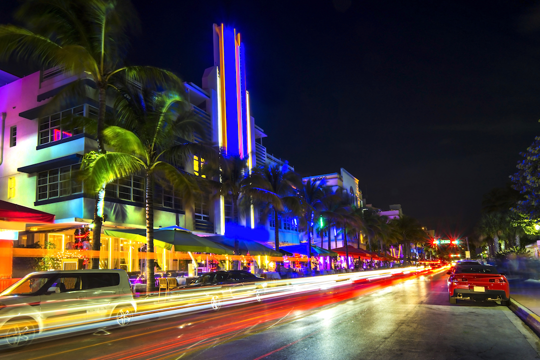 Photo taken at night, on Miami Beach, with famous art deco hotels on background and palm trees.
