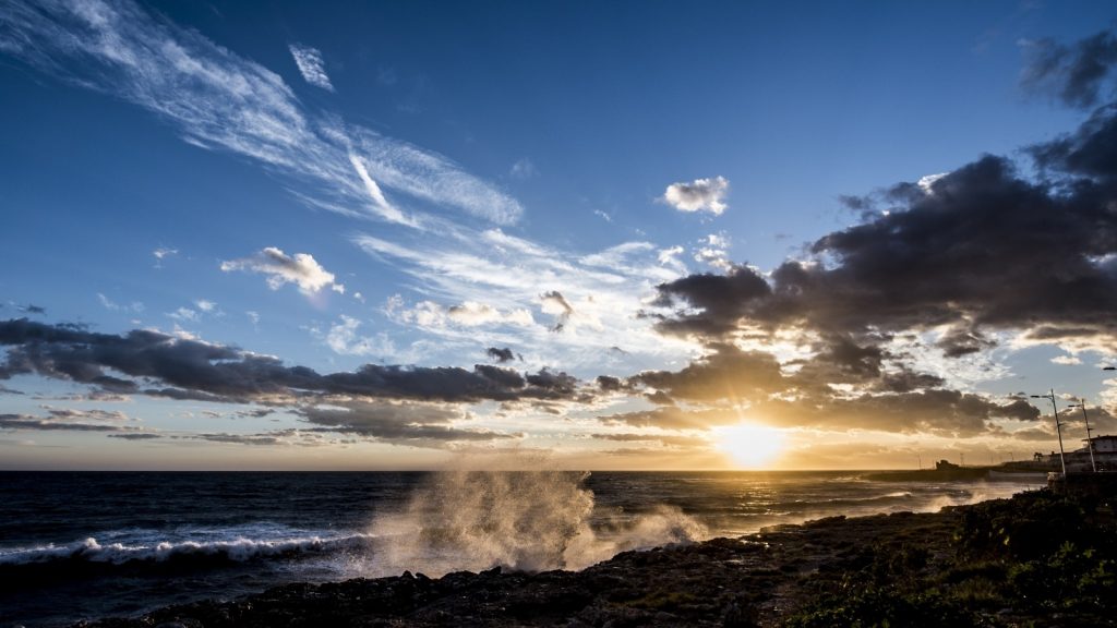 sun rising out of the sky through the clouds under a blue sky over a dimly lit beach