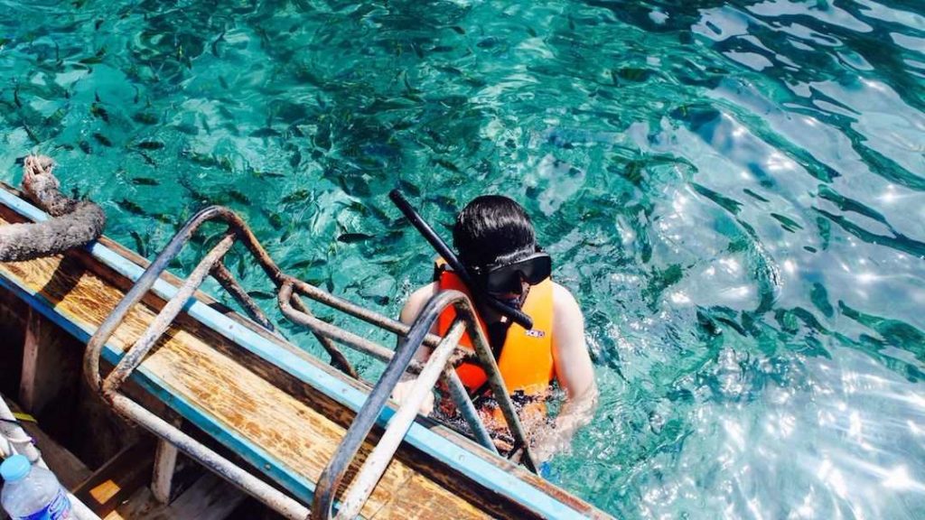 person by a boat wearing a snorkel about to submerge herself