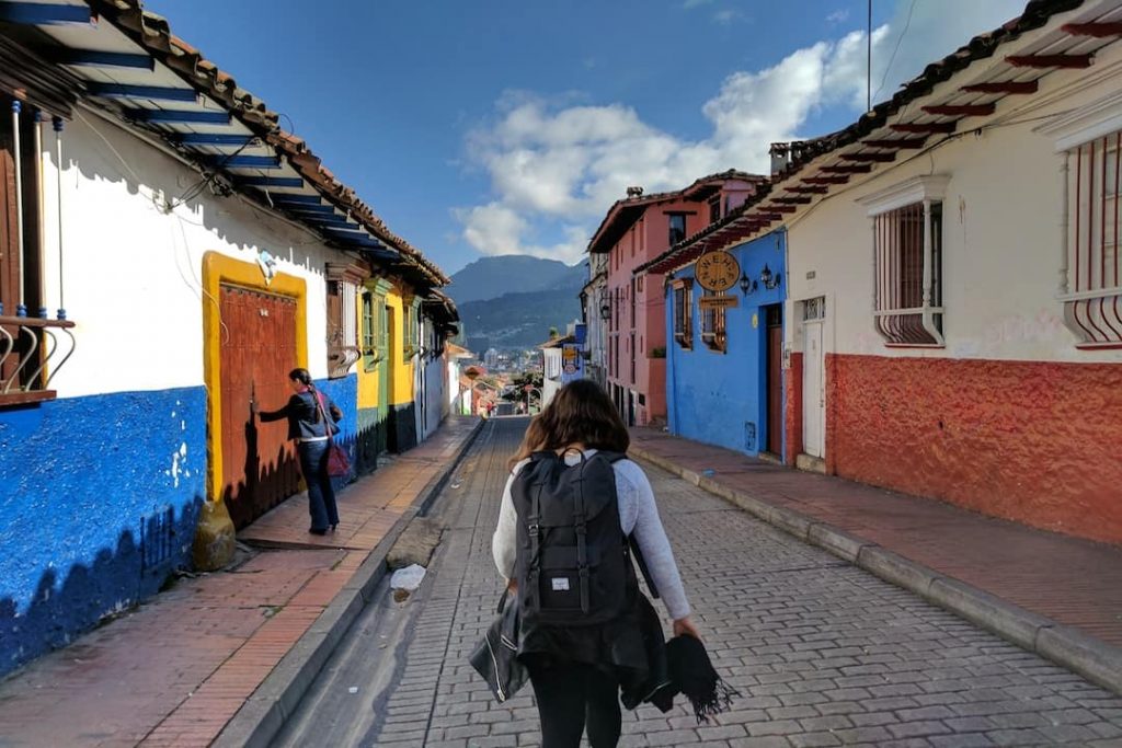 A tourist with a backpack wanders through a colourful alleyway in Bogota