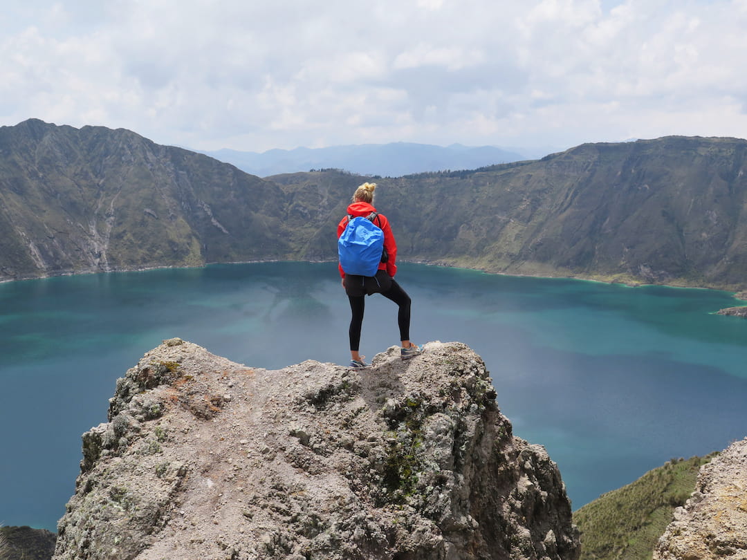 A girl stand on a rock overlooking a massive lake in a valley in Ecuado