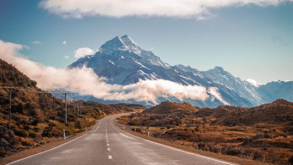 A road surrounded by fields leading through the mountains of New Zealand