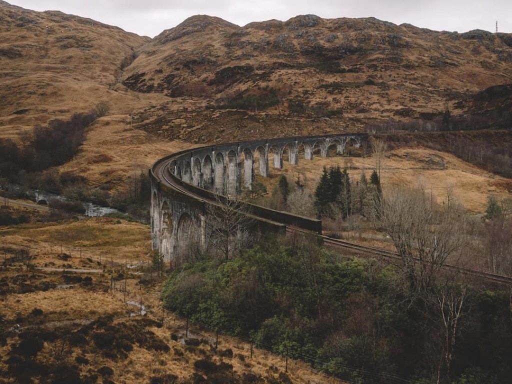 Ireland Vs Scotland: a stone train track with arches winds through scottish countryside