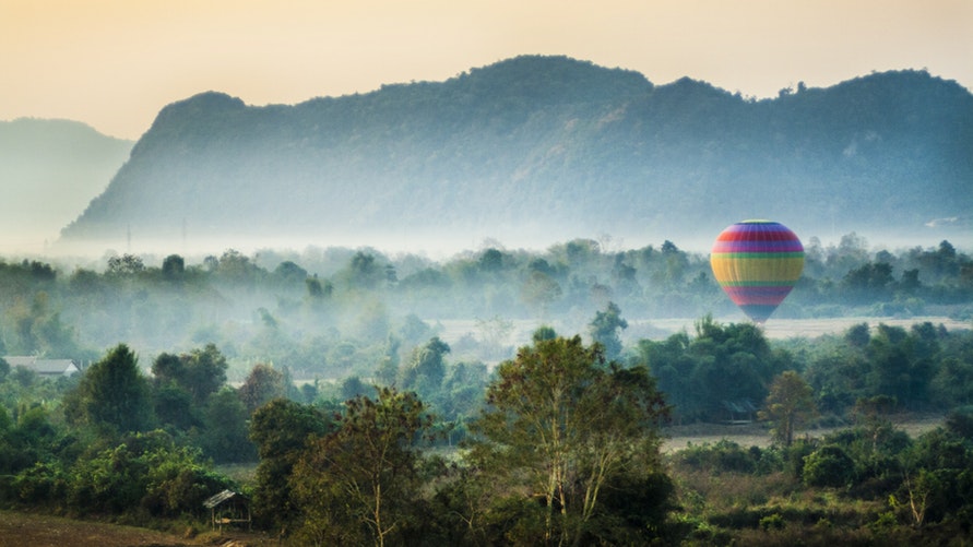 A hot air balloon hovers in a field with green trees