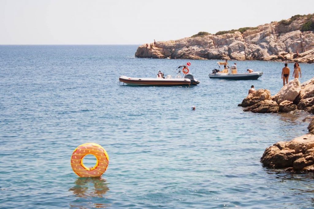 People in boats by a rock - Summer in Greece