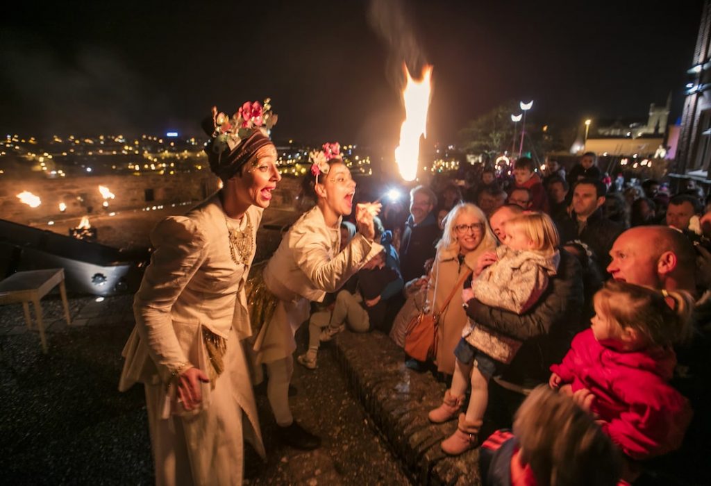 Two performers doing tricks with fire in front of a crowd on Halloween at night