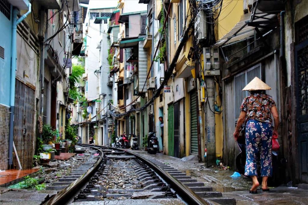 a woman walks on a narrow street beside train tracks in Hanoi, Vietnam
