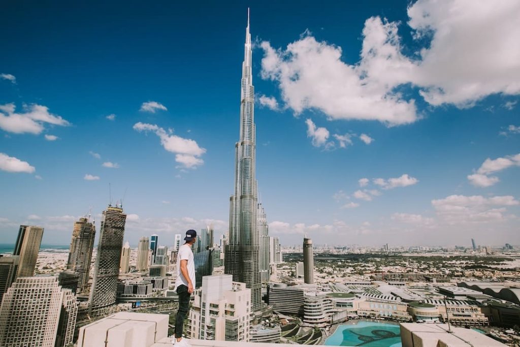A man standing on the ledge of a building in Dubai with Burj Khalifa in the background