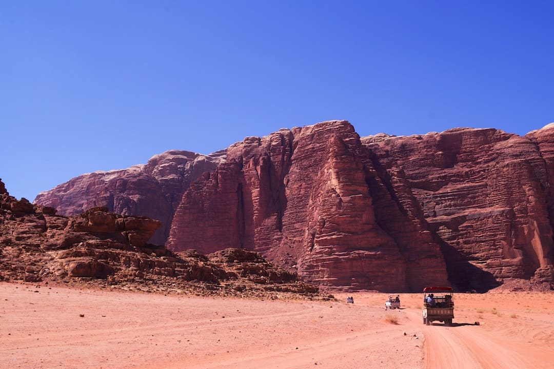 A series of vehicles driving towards a moutain in Wadi Rum, Jordan