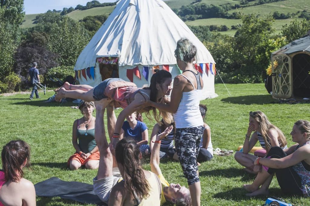 a blue-haired woman helps two people balance on each other at the sun and moon yoga festival