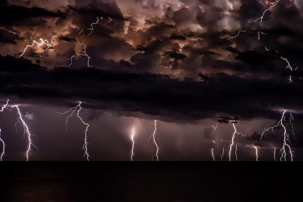 several bolts of lightning cracking into the ocean on a dark, gloomy night