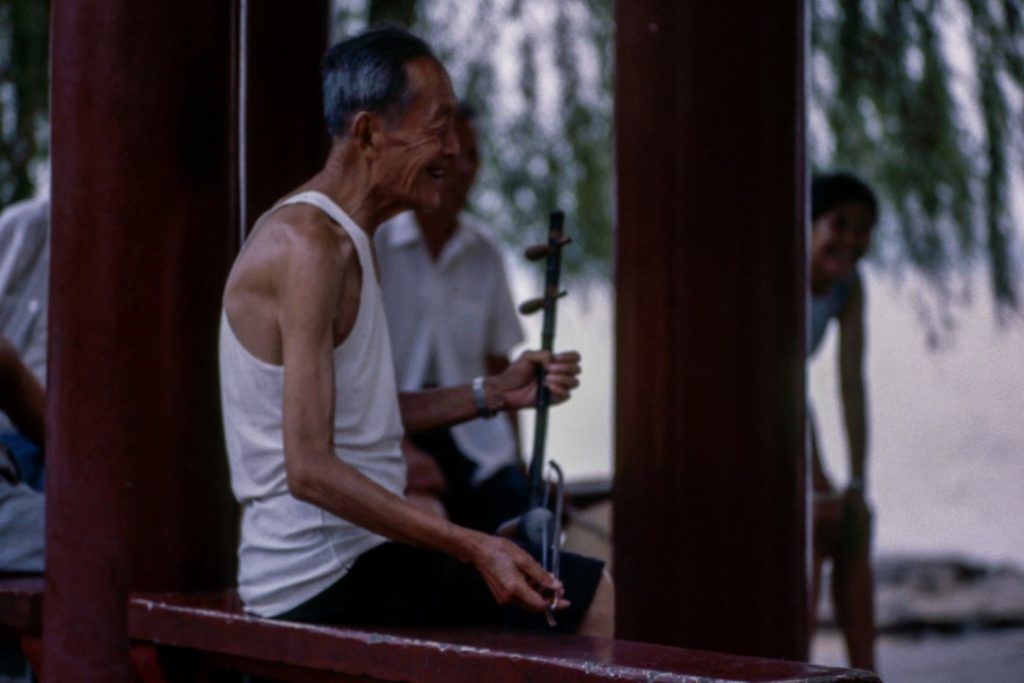 An older man with his back facing the camera plays a string instrument
