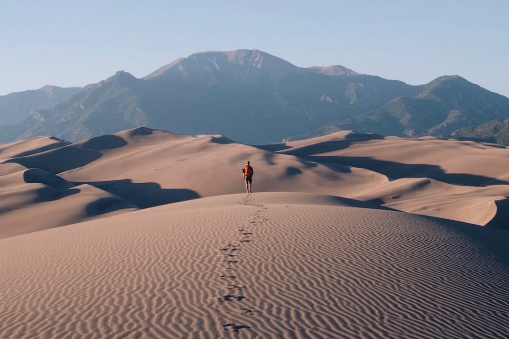 A lone hiker hits the sand dunes in a desert
