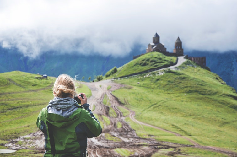 A girl takes a picture of a castle in the mountains