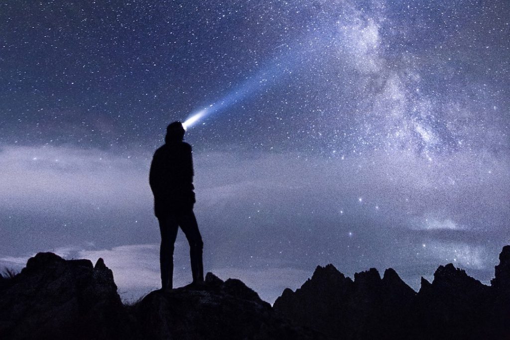 a hiker with a headlamp gazes into the nighttime sky