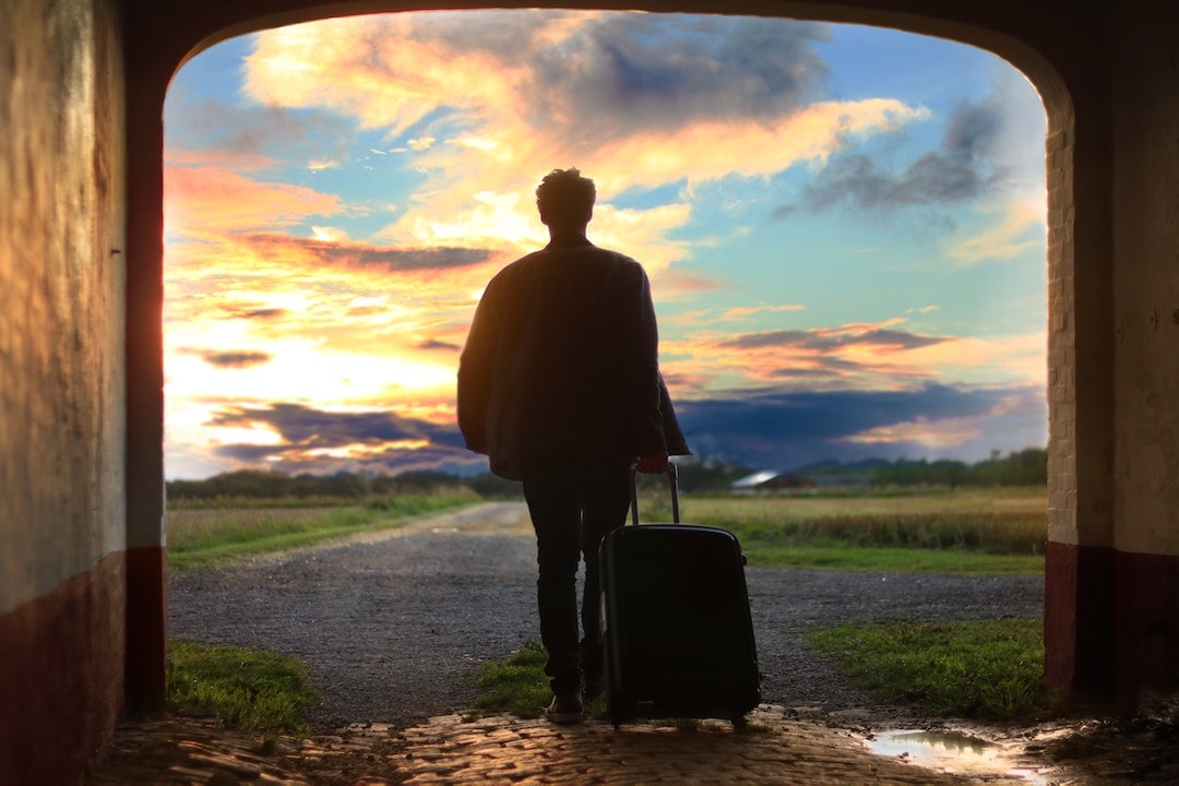 A person standing in front of a gravel road dragging a suitcase