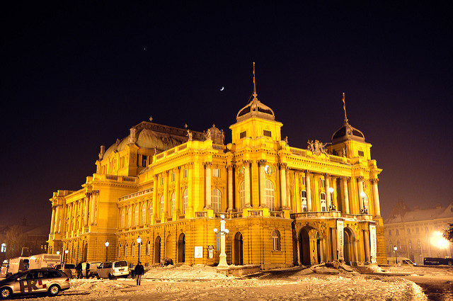 A brightly lit Croatian National Theatre against a purple sky surrounded by snow