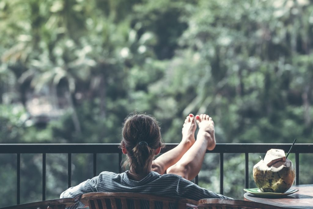 person sitting on chair in front of tree sipping a coconut