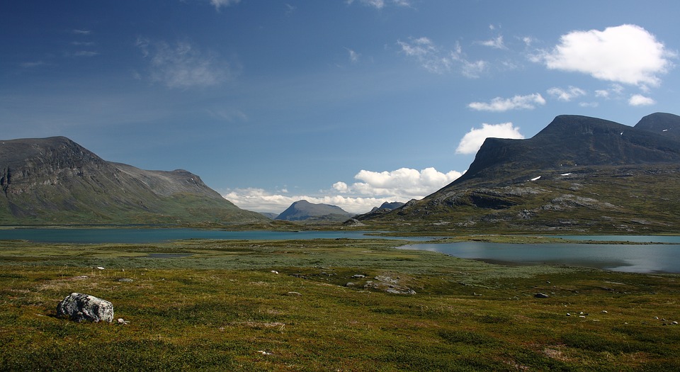 an aquamarine water body surrounded by peaks and green grass