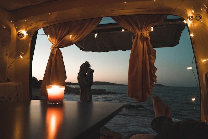 The view from the back of a van with the windows opened; the ocean and christmas lights hanging around the van
