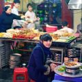 a girl sitting in front a market stall eating a meal on a low set table