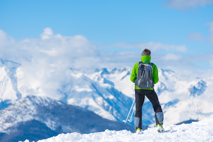 A person in a green jacket standing at the top of a ski slope