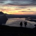 two people looking in the sunset overlooking a lake and a cliff