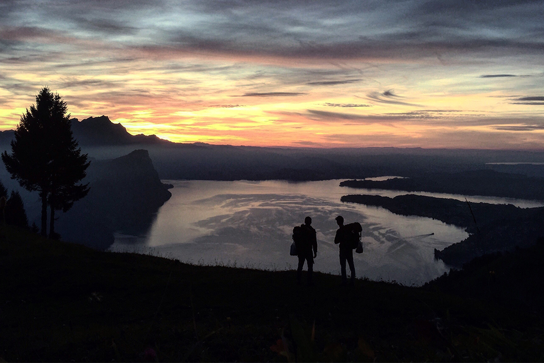 two people looking in the sunset overlooking a lake and a cliff