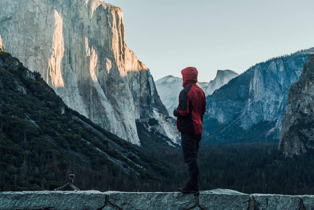 A person in a red coat standing by El Capitan in Yosemite National Park, California