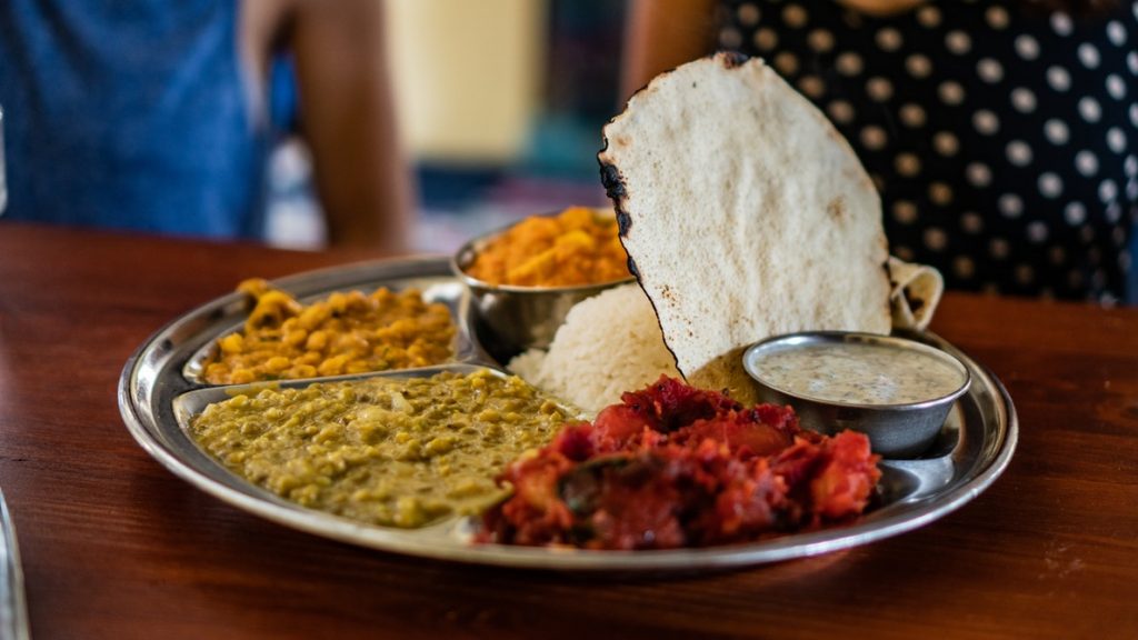 a round silver Indian thali dish with different curries, white rice and other foods