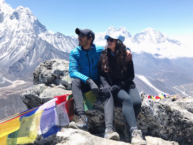 a couple sitting on a rock with the himalayas in the background