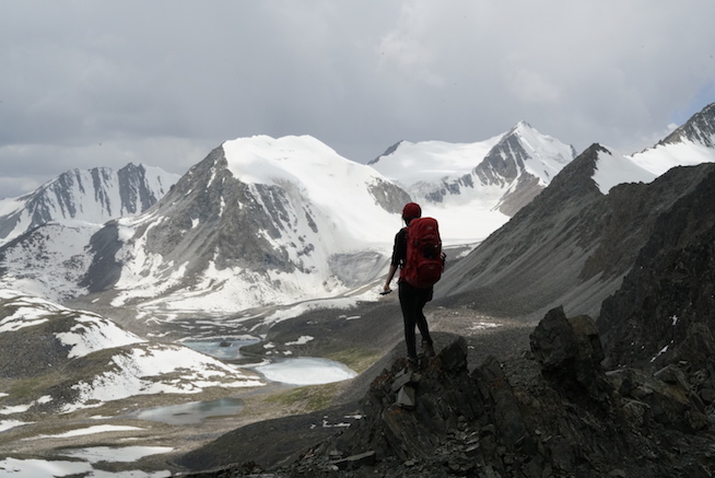 girl with a red backdrop hiking snowcapped mountains