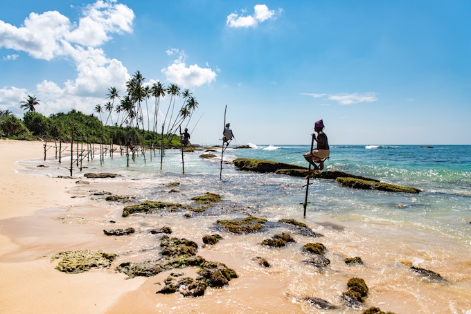 people balancing on poles on a beach in Sri Lanka