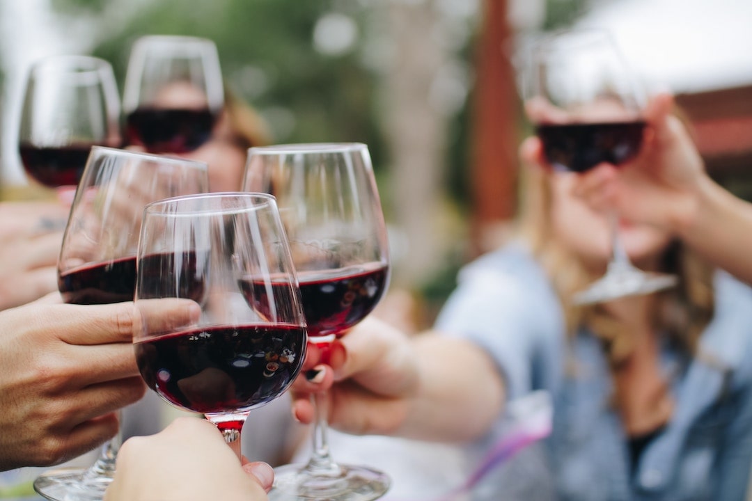 A group of people toasting with glasses full of red wine