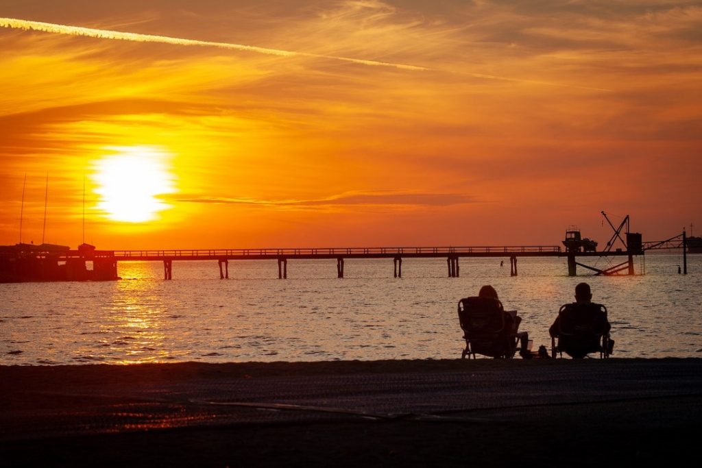 Couple sitting on the beach at sunset at Kitsilano Beach, Vancouver, Canada
