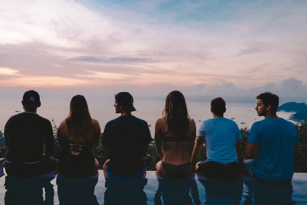 a group of six people at sunset sitting on an infinity pool