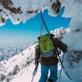 A man wearing a green backpack carrying skis walking through an ice tunnel