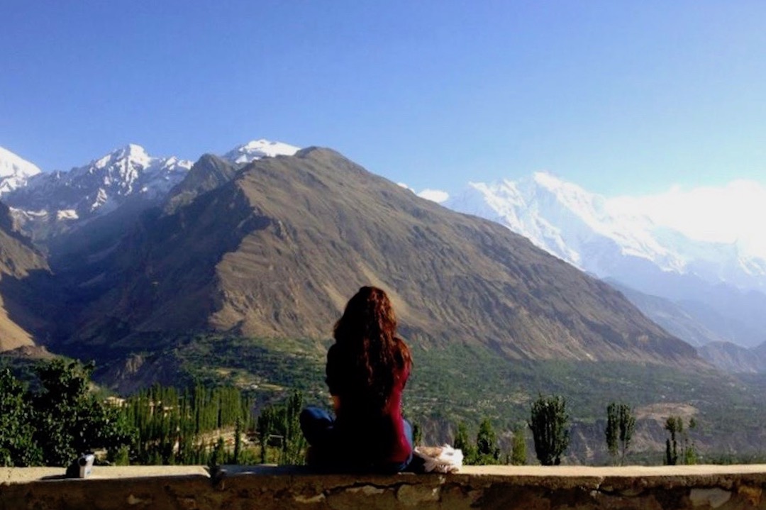 a girl sitting on a wall overlooking a mountain