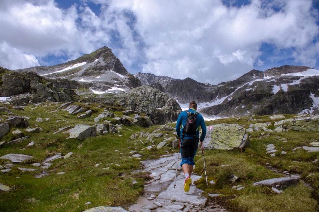 Man hiking with trekking poles along a path with mountains in the background