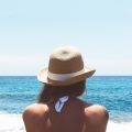 Woman standing on a beach facing the ocean wearing a hat