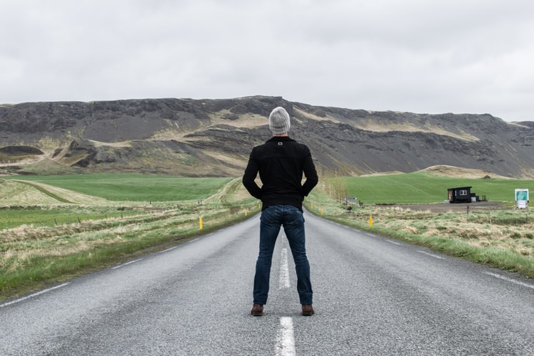man standing in the middle of a road with green scenery off in the distance