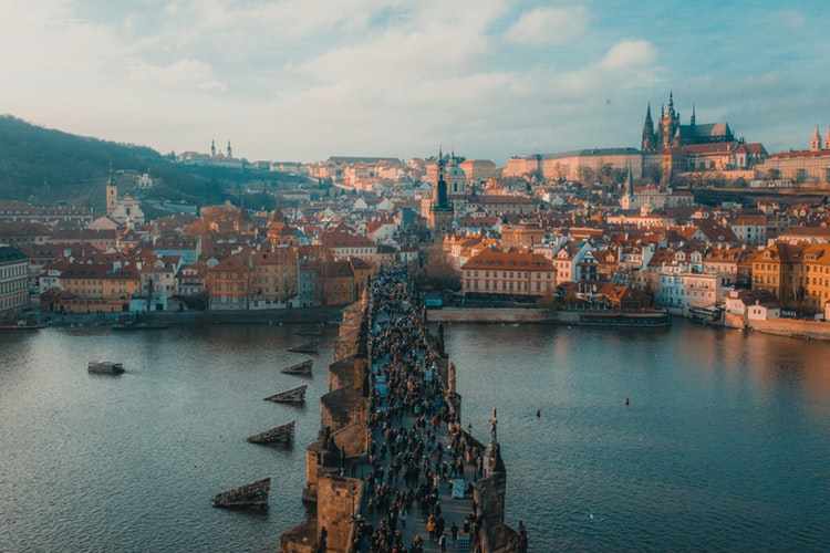people walking on bridge over the river with an old landscape in the background
