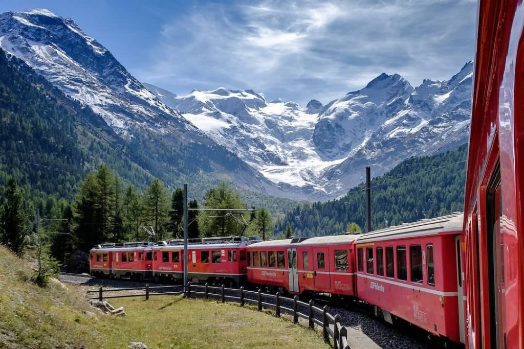 A red train travelling along forest and mountain peaks in Switzerland