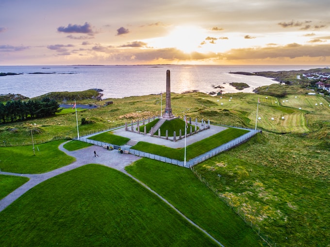a grey pillar landmark beside the sea surrounded by green grass