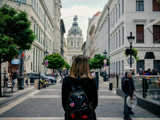 a girl with a backpack standing in the middle of a city
