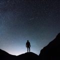Person standing on a mountain looking up at the starry night sky
