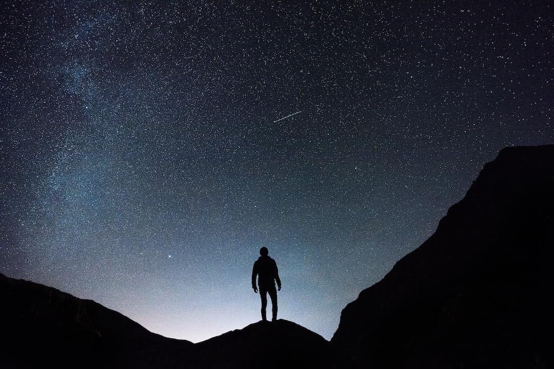 Person standing on a mountain looking up at the starry night sky