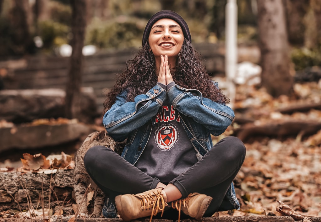 a girl smiling as she sits crosslegged and meditates with her hands in prayer