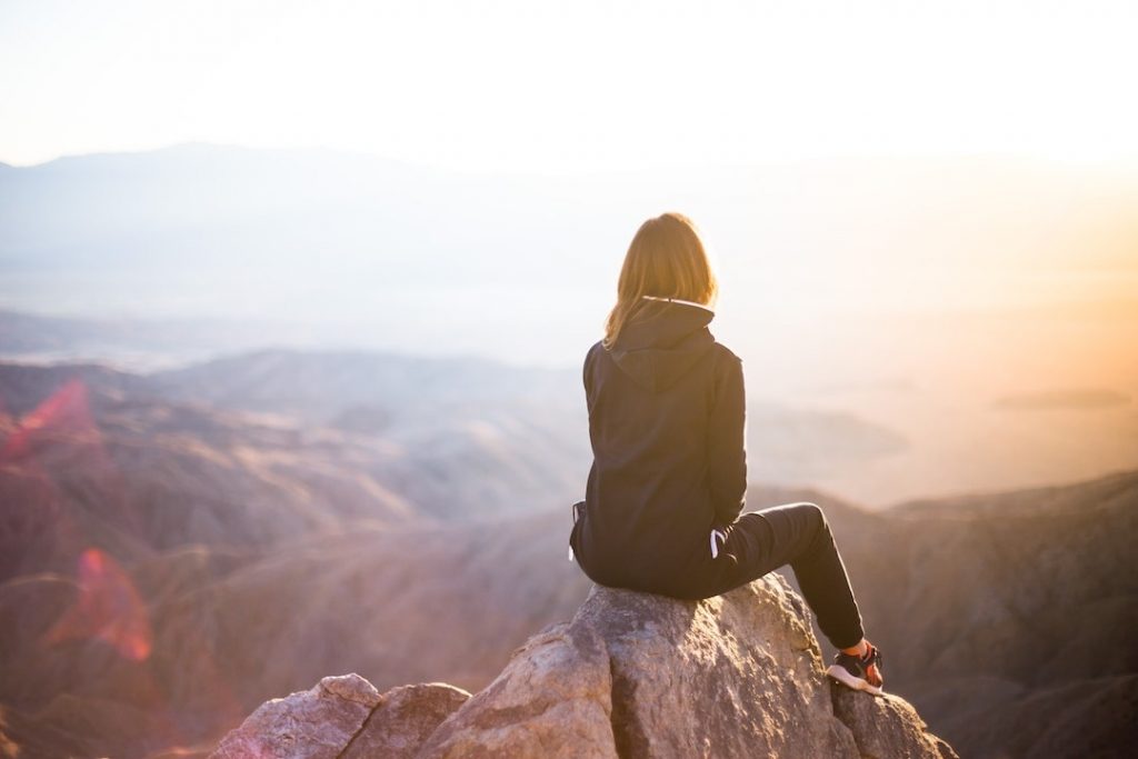 Woman sitting at the top of a mountain overlooking scenic lookout